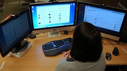 Unha muller traballa diante de varias pantallas de ordenador utilizando varios programas diferentes