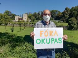 Manuel Monge cun cartel no que se le "Fóra Okupas" e ao fondo o Pazo de Meirás / remitida