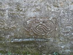 Pedra cun motivo decorativo formado por un complexo entrelazado en altorrelevo, cun círculo na parte superior e dous círculos máis na inferior, atopado na Igrexa de Santiago da Veiga, en Sarria / Patrimonio dos Ancares