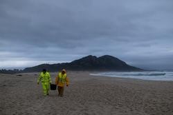 Dous homes cargan un cubo cheo de pellets, na praia Do Dique, a 13 de xaneiro de 2024, en Queiruga / Elena Fernández - Arquivo