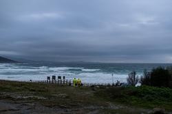 Dous homes cargan un cubo cheo de pellets, na praia Area Maior, a 13 de xaneiro de 2024, en Muros, A Coruña, Galicia.. Elena Fernández - Europa Press / Europa Press